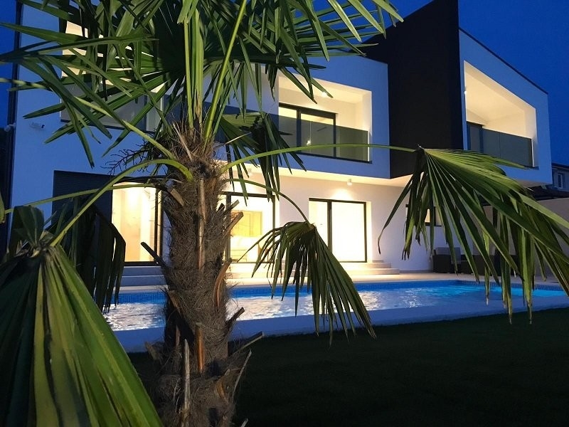 Villa illuminata con piscina dietro la palma alla sera