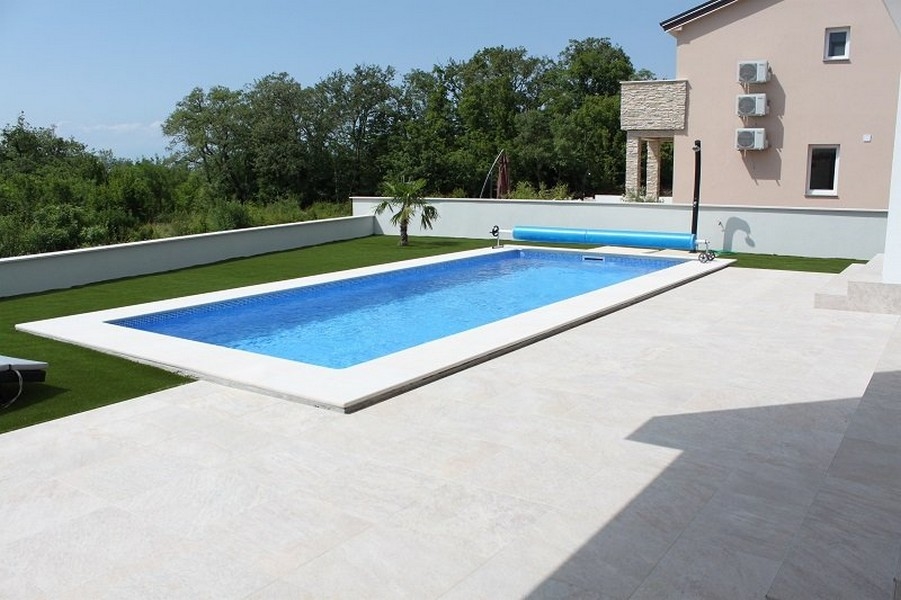 Lunga piscina sulla terrazza piastrellata accanto al prato