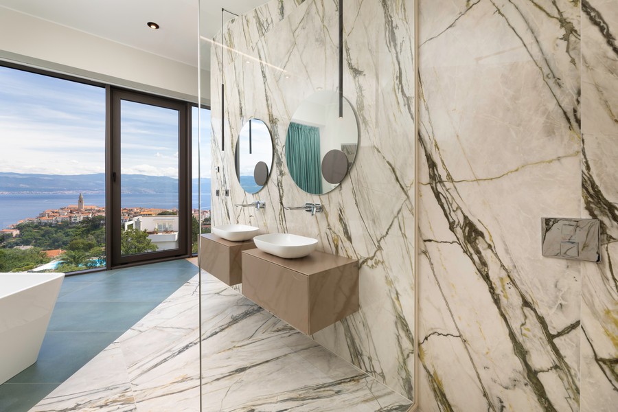 Doppio lavabo davanti alla parete in marmo con specchi rotondi