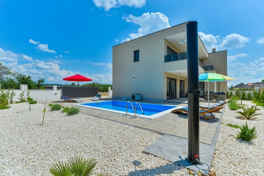 Villa con piscina e ombrelloni nel giardino di ghiaia