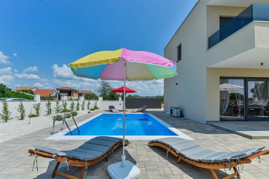Piscina con ombrelloni colorati e lettini accanto alla casa bifamiliare