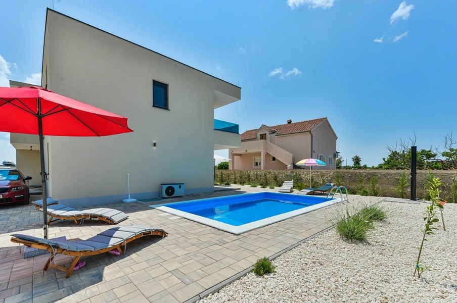 Piscina con lettini e ombrellone rosso accanto alla casa