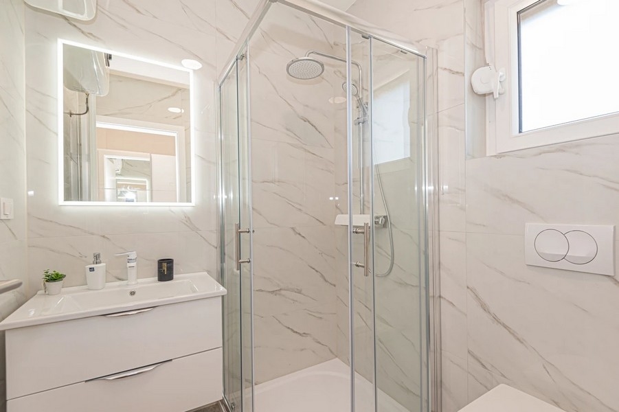Bagno effetto marmo con doccia ad angolo e specchio illuminato