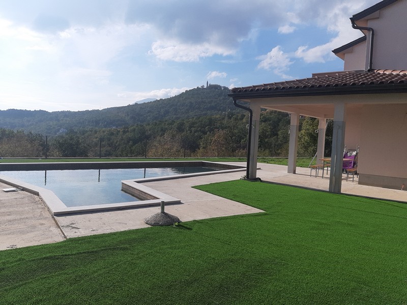 Piscina con prato sintetico e terrazza davanti alle colline boscose