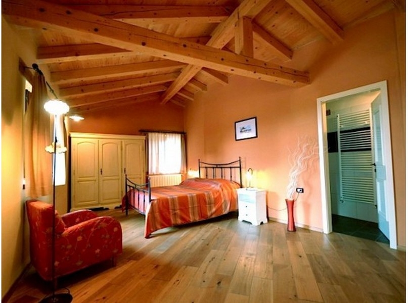 Camera da letto con travi in legno, letto in ferro e accesso al bagno