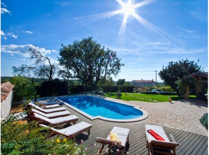 Piscina con lettini sotto un albero in controluce