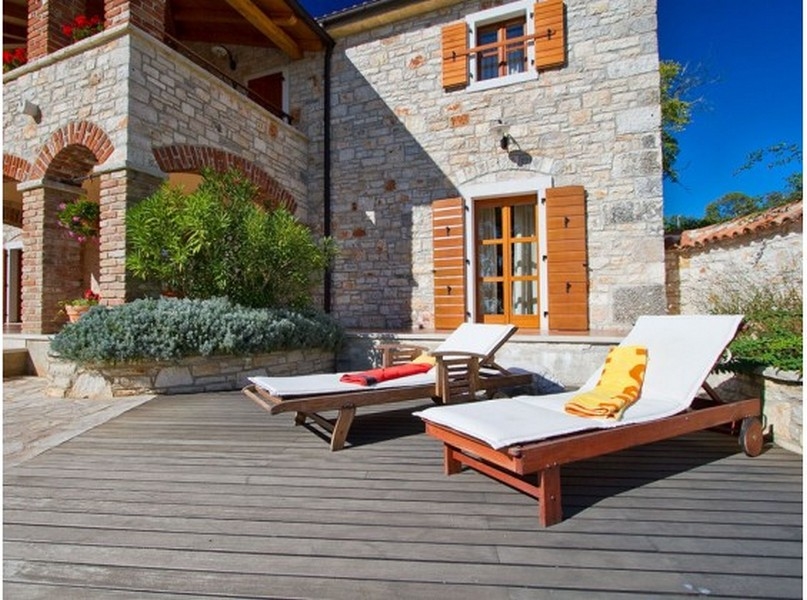 Terrazza in legno con lettini davanti alla facciata in pietra naturale