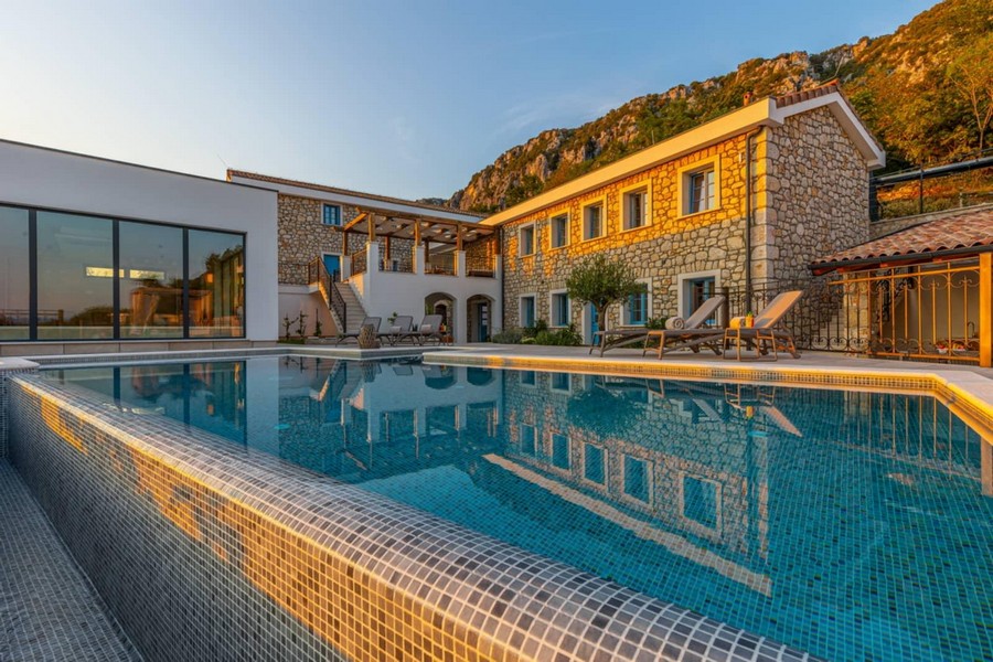 Piscina davanti alle case in pietra alla luce della sera sotto la parete rocciosa