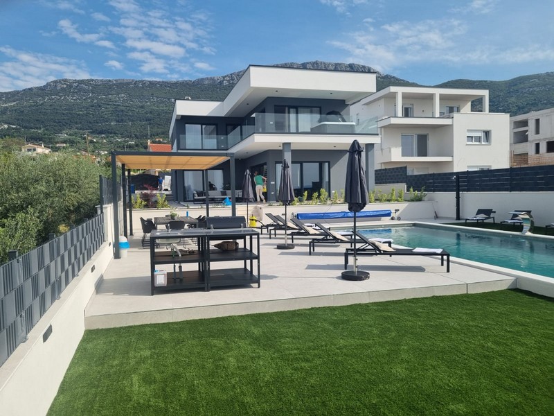 Prato sintetico e terrazza della piscina con pergola davanti alla catena montuosa