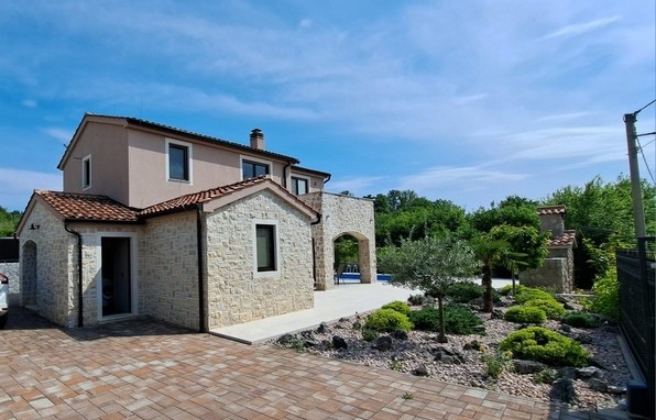 Casa con facciata in pietra naturale e aiuola di ghiaia con ulivo