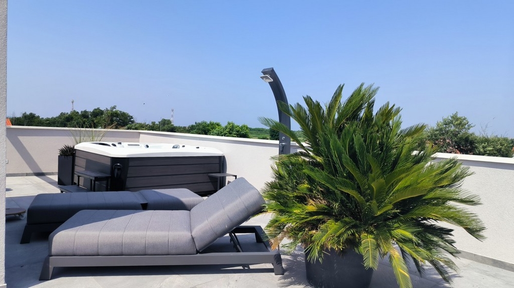 Terrazza sul tetto con lettino, vasca idromassaggio e vista sul verde.