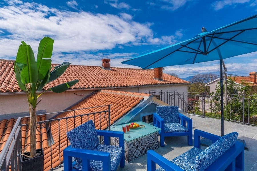 Terrazza sul tetto con mobili blu e ombrellone sopra le tegole