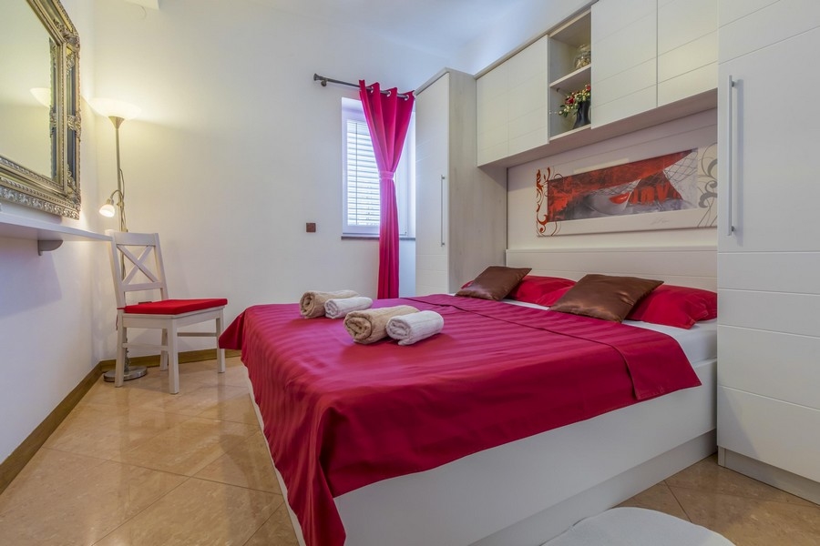 Camera da letto con copripiumino rosso e mobili bianchi in una casa plurifamiliare croata sul mare