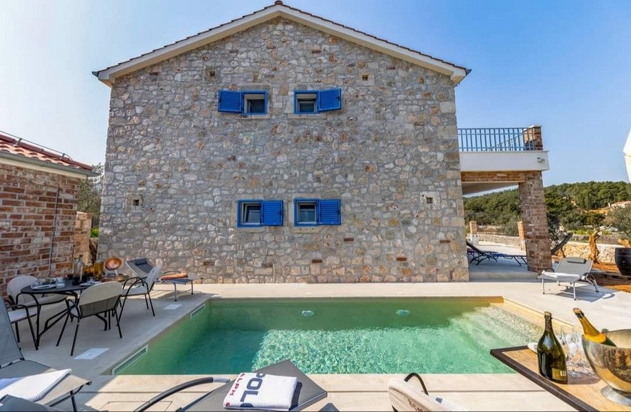 Vista posteriore di una villa in pietra croata in vendita con piscina privata e area barbecue.