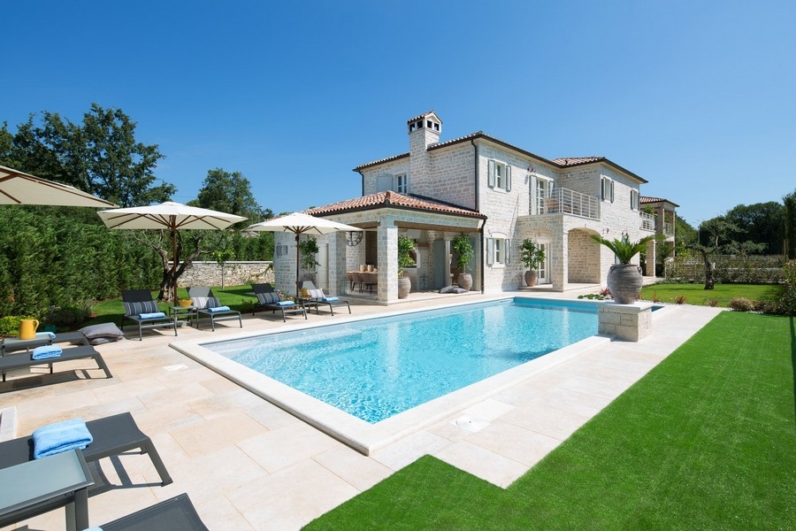Vista luminosa e soleggiata di una villa croata con piscina, ombrelloni e sdraio.