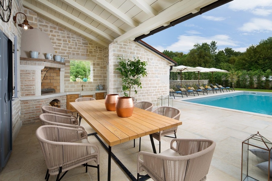 Zona pranzo esterna coperta con tavolo in legno a bordo piscina in una villa