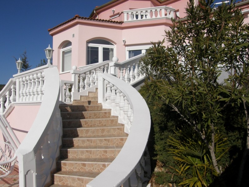 Vista frontale della villa rosa in Croazia con scala bianca a chiocciola e vegetazione mediterranea