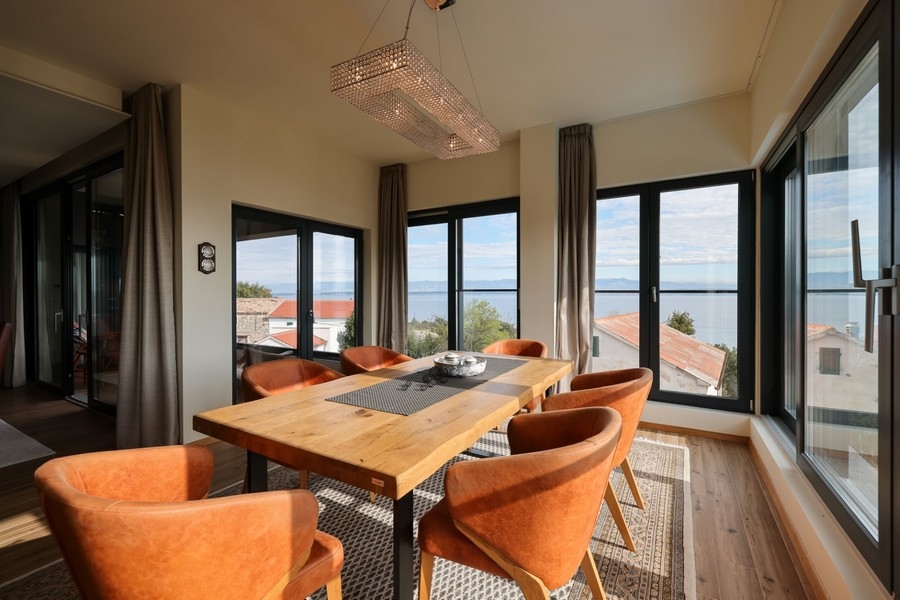 Zona pranzo con tavolo in legno, sedie arancioni e vista mare