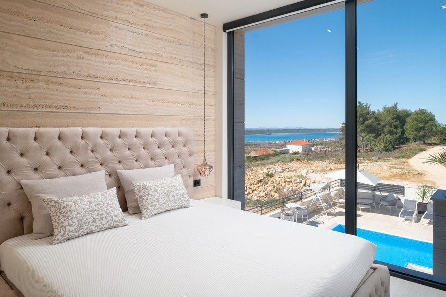 Elegante camera da letto in una villa in vendita a Razanac, zona di Zadar, Croazia, con letto grande con testiera, vista mare e accesso all'area piscina.