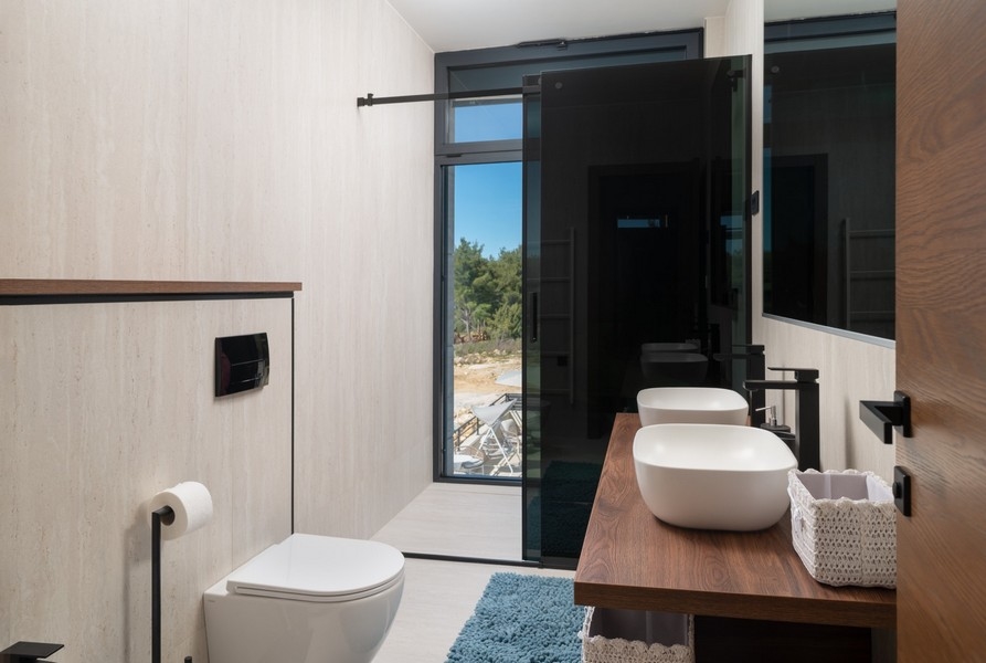 Bagno elegante con vista mare in una villa in vendita a Razanac, zona di Zadar, Croazia, dotato di WC sospeso e di un moderno lavabo da appoggio su un mobile in legno.