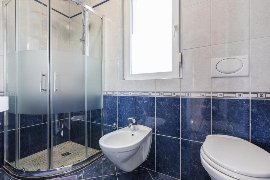 Bagno in un immobile in Croazia, casa plurifamiliare con vista mare, con doccia ad angolo, bidet e WC, pareti chiare e piastrelle blu scuro