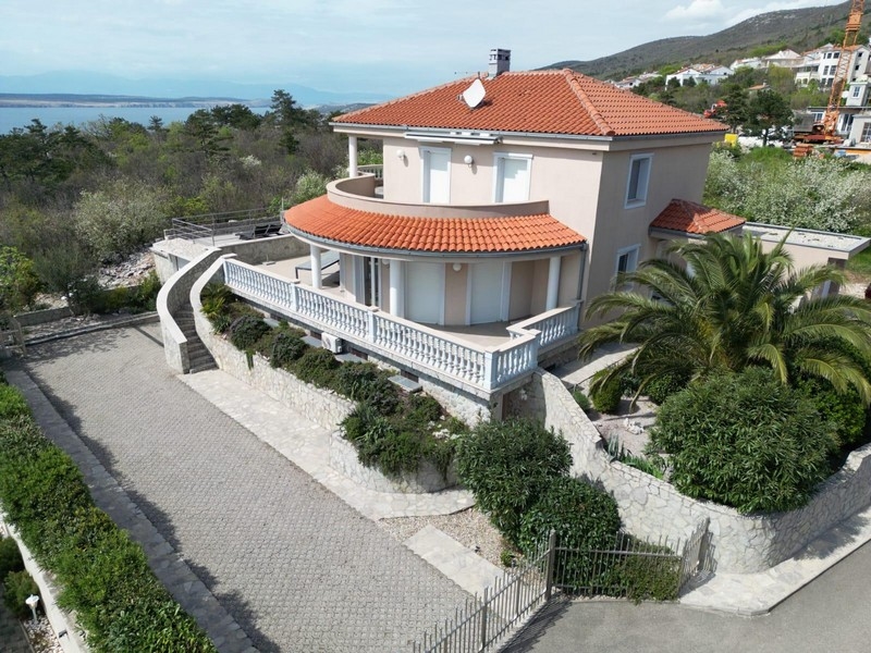 Vista esterna di una casa plurifamiliare croata con tetto rosso e balcone, circondata da aree verdi