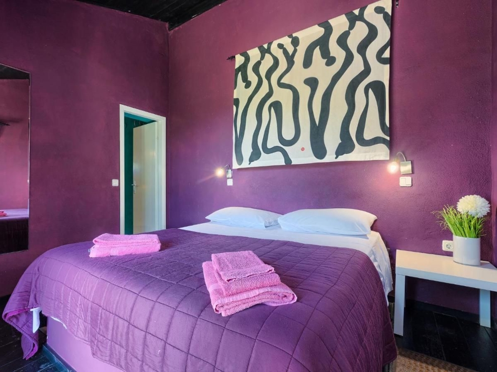 Una camera da letto in un immobile in Croazia, con pareti viola, un grande dipinto con motivi astratti, due lampade da comodino e biancheria in tinta viola