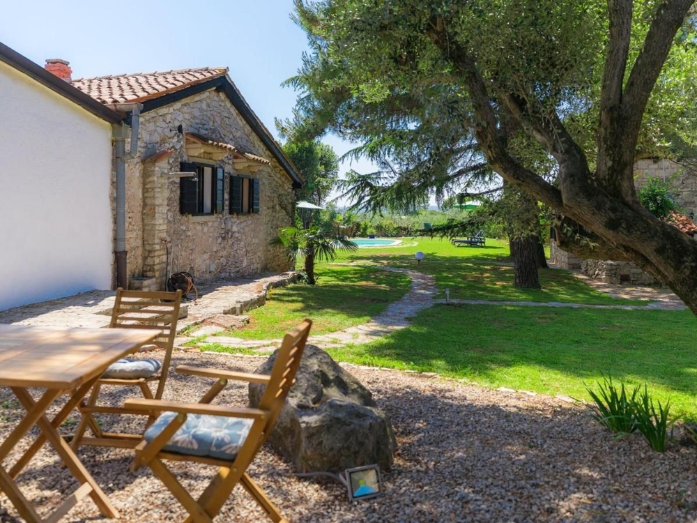 Sentiero attraverso un giardino ombreggiato conduce a un grazioso edificio in pietra, tipico di immobili in Croazia
