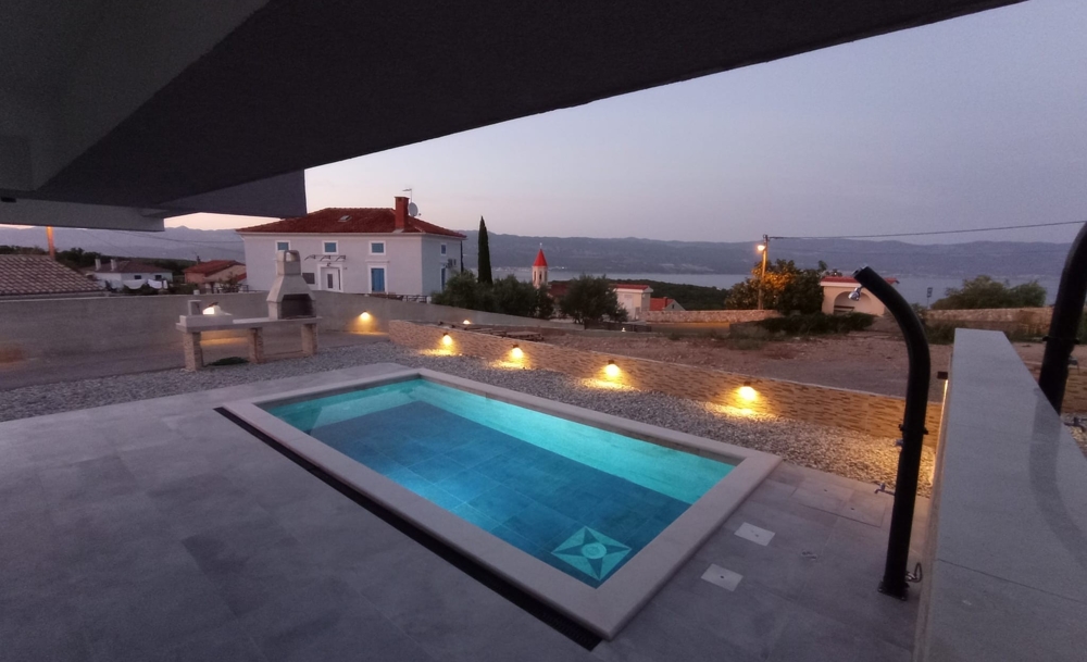 Vista serale di un immobile in Croazia con piscina illuminata e vista sul mare sullo sfondo.