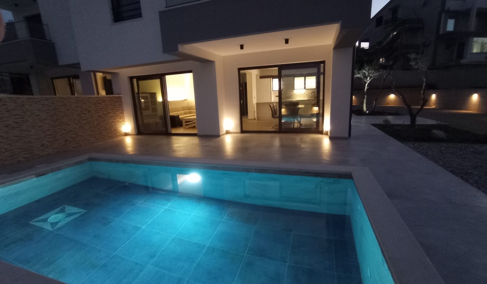 Vista al crepuscolo della terrazza e della piscina di un immobile in Croazia, l'illuminazione interna crea un'atmosfera accogliente.