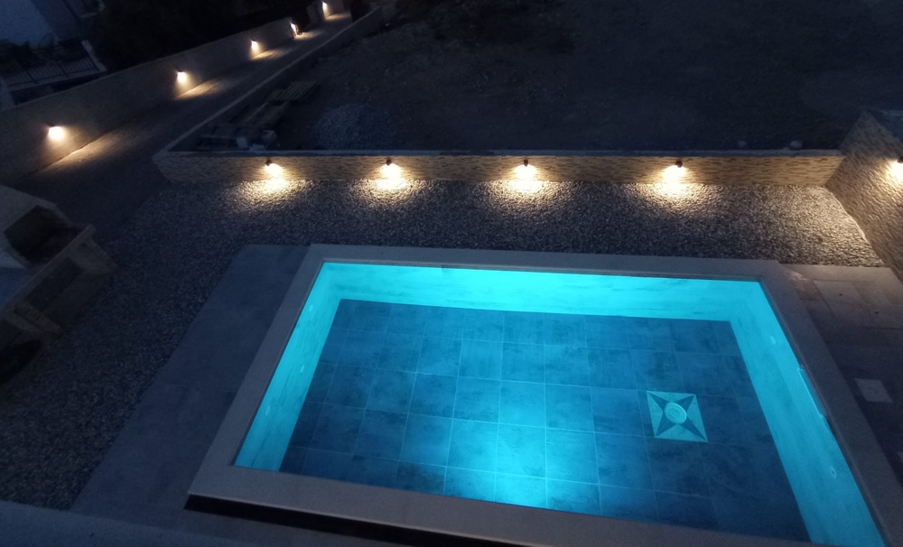 Vista notturna di una piscina con illuminazione blu e vista parziale dell'immobile in Croazia sullo sfondo.