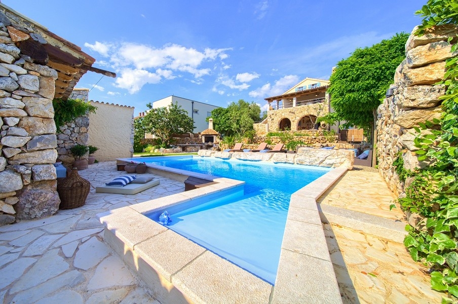 Piscina con terrazza in pietra naturale e vista sulla casa in pietra