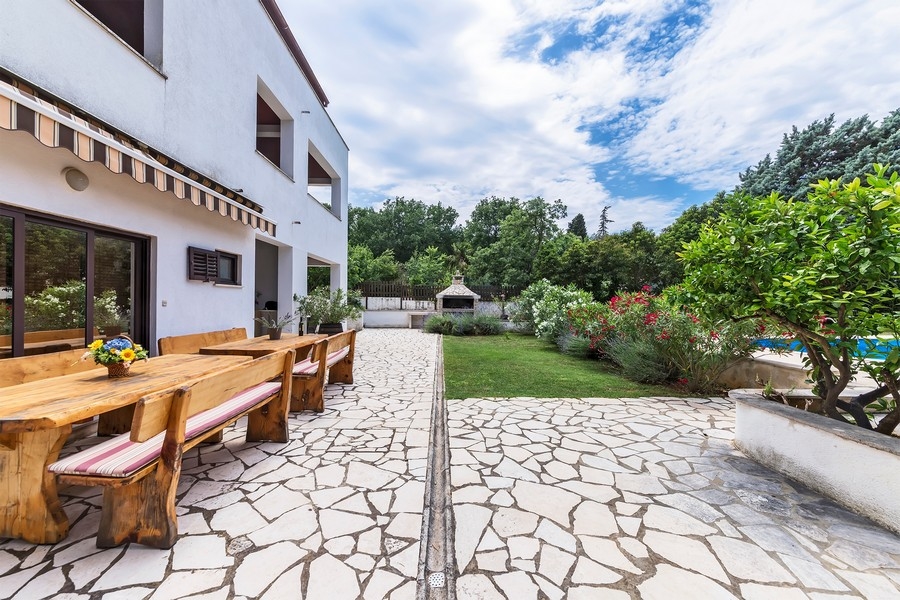 Immobili Croazia, casa plurifamiliare in Istria con vista mare - Panorama Scouting H3025: una terrazza con un lungo tavolo in legno e panche, circondata da un giardino curato