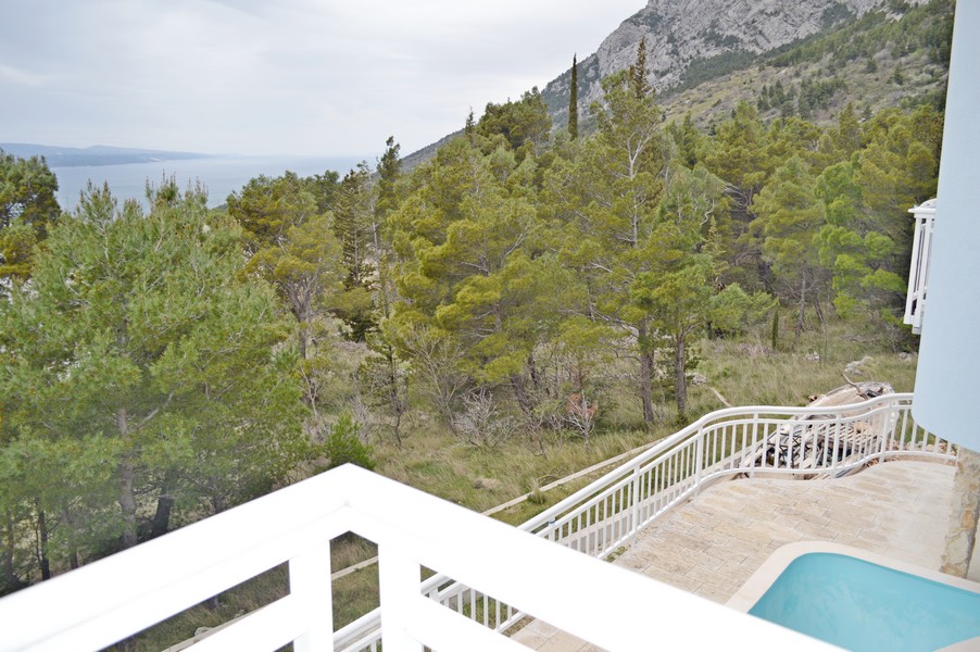 Vista dal balcone oltre i pini fino al mare e alla parete rocciosa