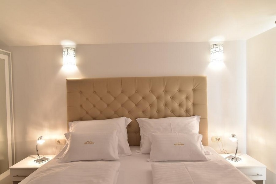 Primo piano del letto nella camera con illuminazione moderna, offerto dall'agenzia immobiliare Panorama Scouting