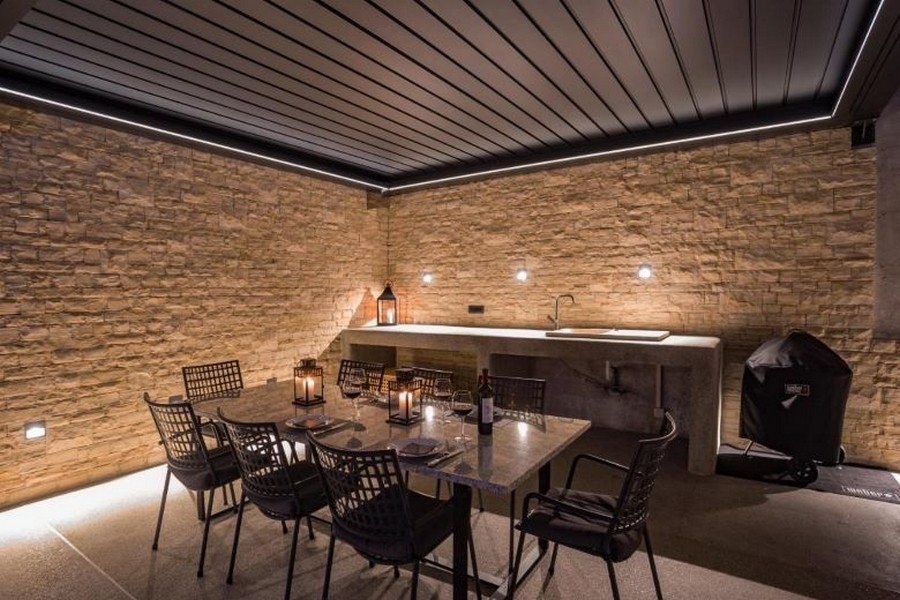 Area esterna coperta con zona pranzo e griglia, circondata da muri in pietra