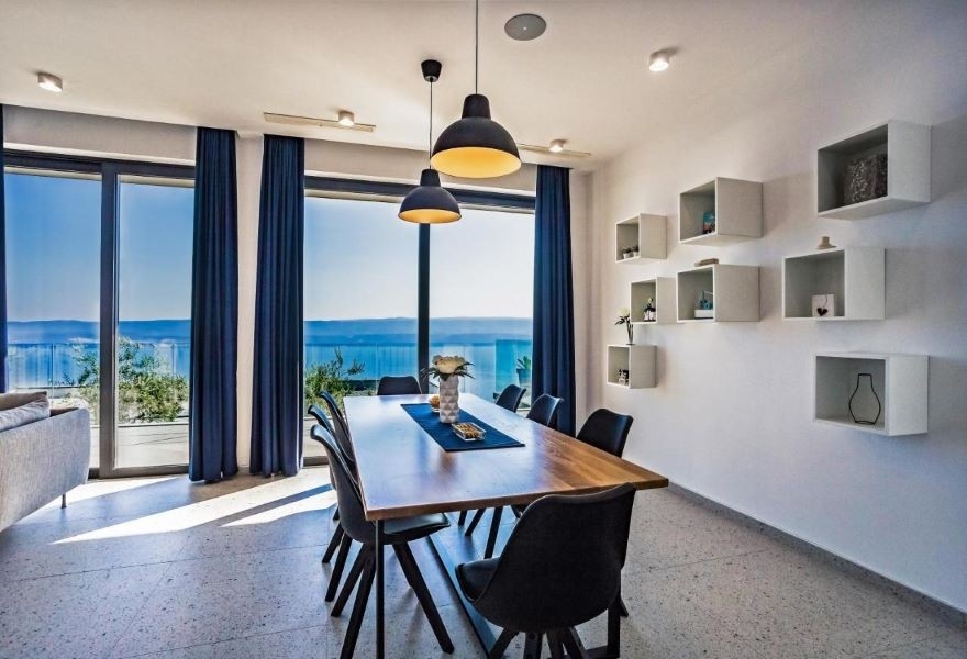 Sala da pranzo con moderno tavolo in legno, sedie nere e vista panoramica sul mare