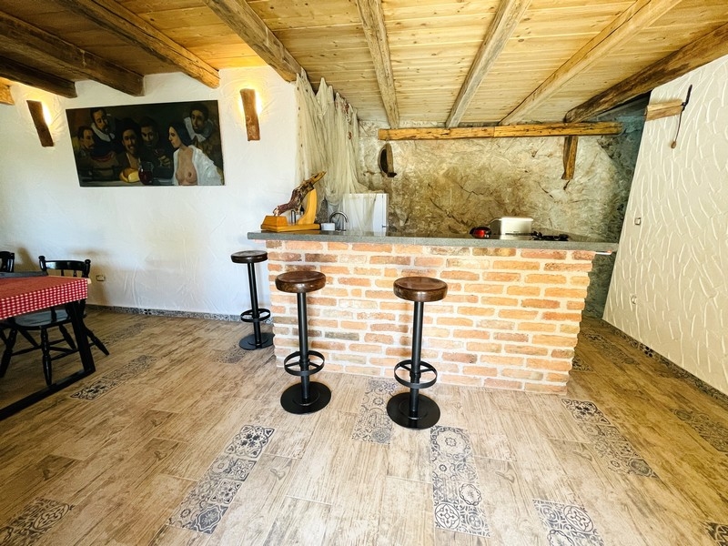 Taverna rustica con bancone in mattoni, soffitto con travi in legno e sgabelli da bar