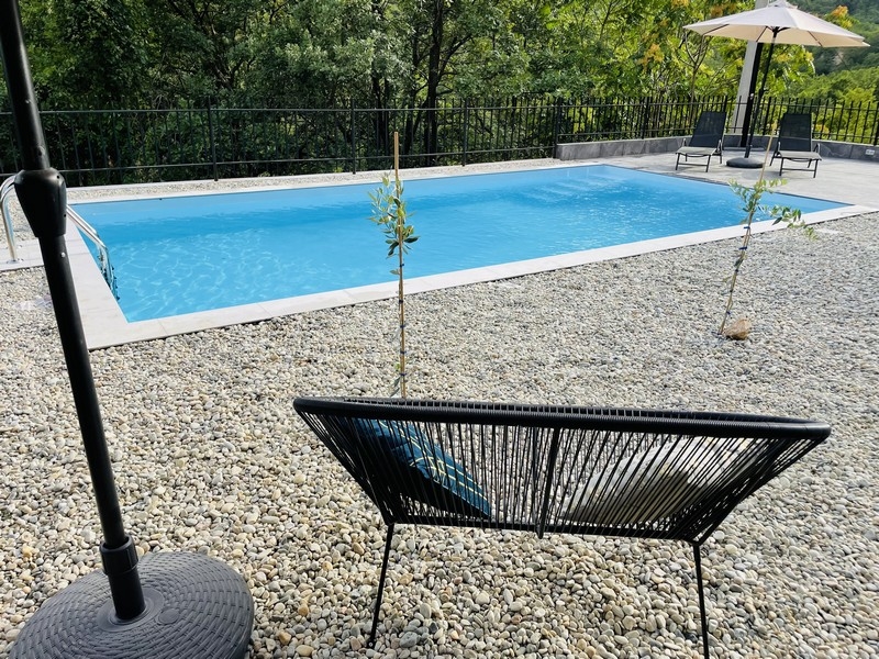 Piscina nel giardino, circondata da ciottoli, con vista sul bosco