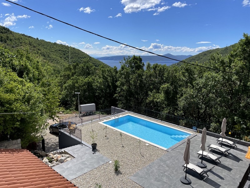 Piscina con lettini tra pendii boscosi con vista mare