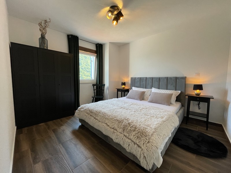 Camera da letto con letto grigio, armadio nero e due comodini, illuminata da luce calda