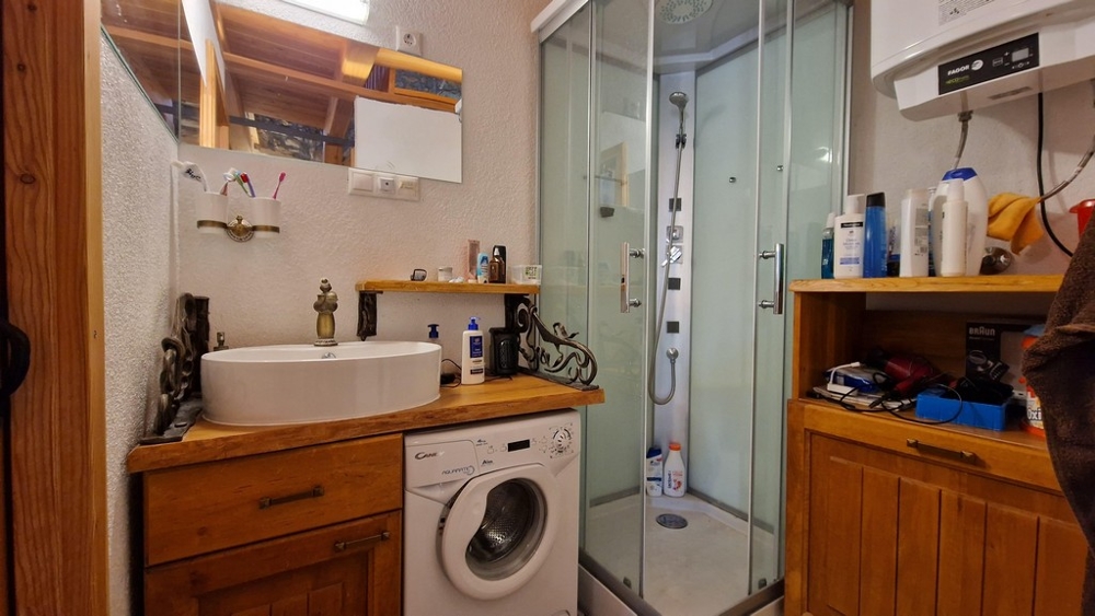 Bagno con box doccia, lavatrice e scaffali in legno.