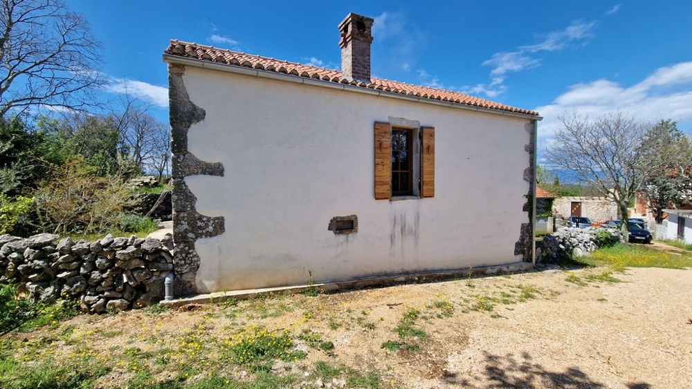 Veduta di una casa mediterranea tradizionale con dettagli in pietra e persiane in legno.