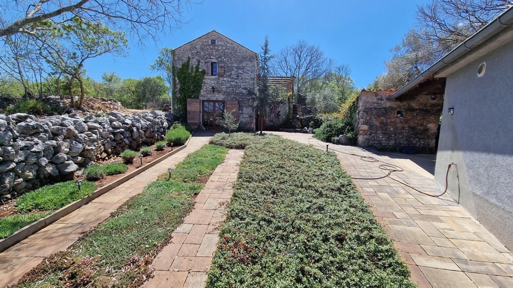 Giardino curato con vialetto lastricato e casa in pietra sullo sfondo.