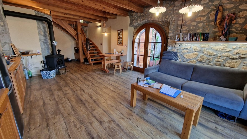Soggiorno aperto con travi in legno, stufa a legna e interni rustici.