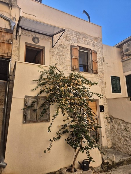 Casa in pietra con persiane in legno e arbusto fiorito nel vicolo