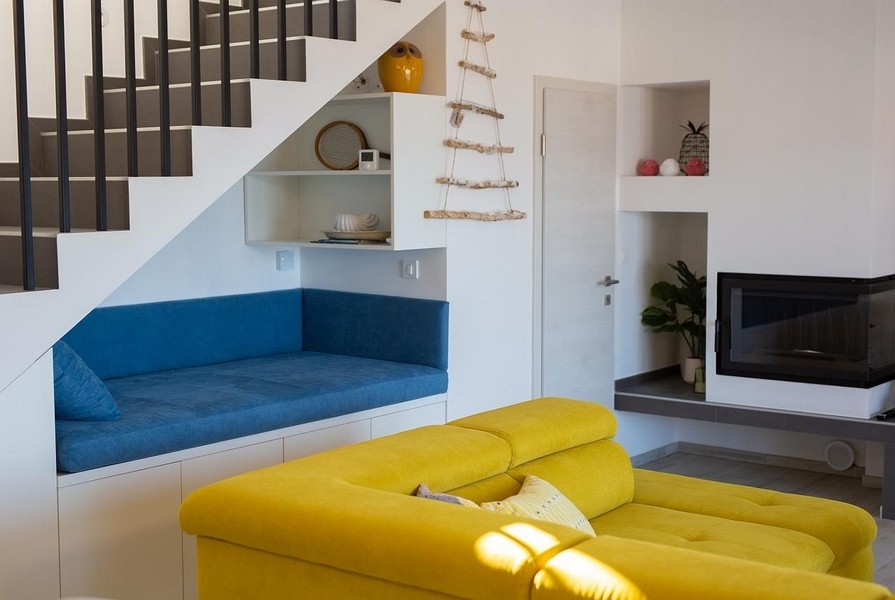Soggiorno con divano giallo, nicchia blu con sedute sotto la scala, design moderno