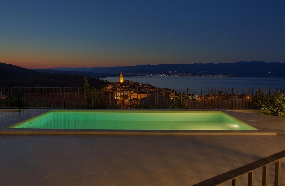 Piscina illuminata di notte e vista su Vrbnik in Croazia.