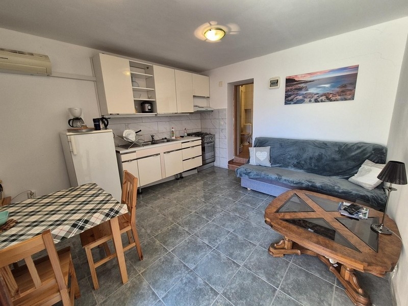 Zona giorno aperta con cucina, tavolo da pranzo e divano, con pavimento piastrellato.