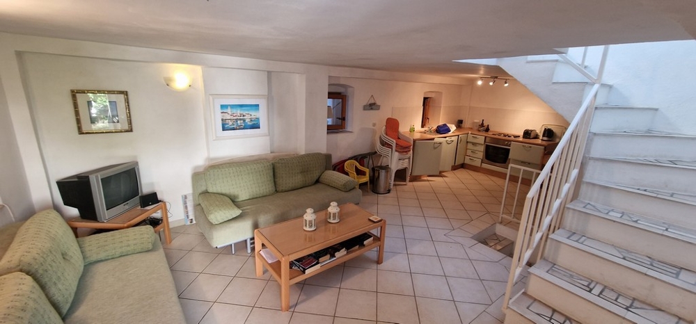 Una zona giorno aperta e accogliente con divani verdi, un tavolino, un televisore e una cucina integrata sullo sfondo. Piastrelle chiare ricoprono il pavimento.